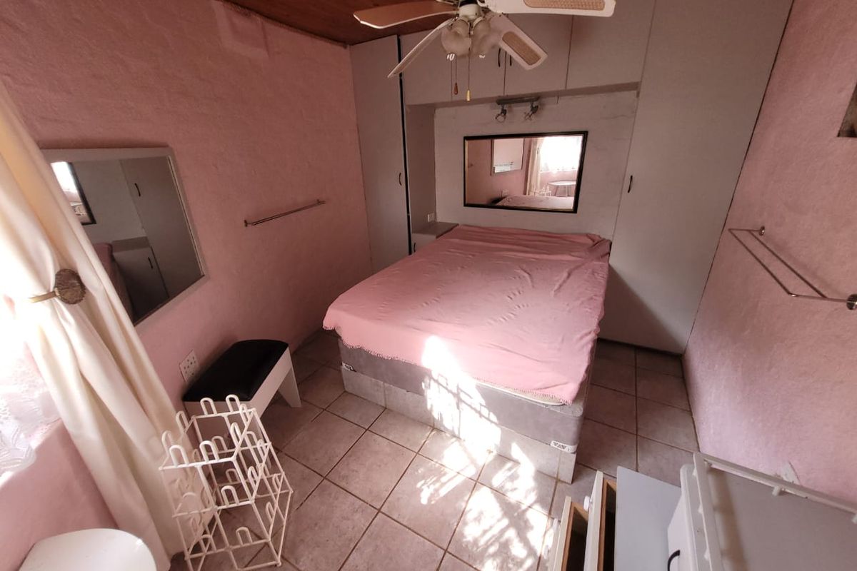 A compact bedroom featuring built-in cupboards, a ceiling fan, and tiled flooring, with a dated aesthetic ready for a modern update.