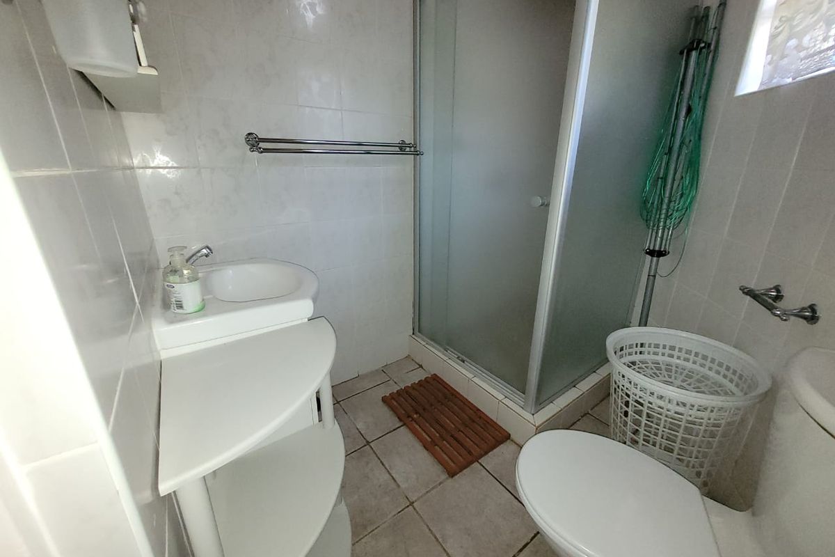 A functional bathroom featuring a shower enclosure, vanity basin, and toilet with neutral tiled finishes throughout.