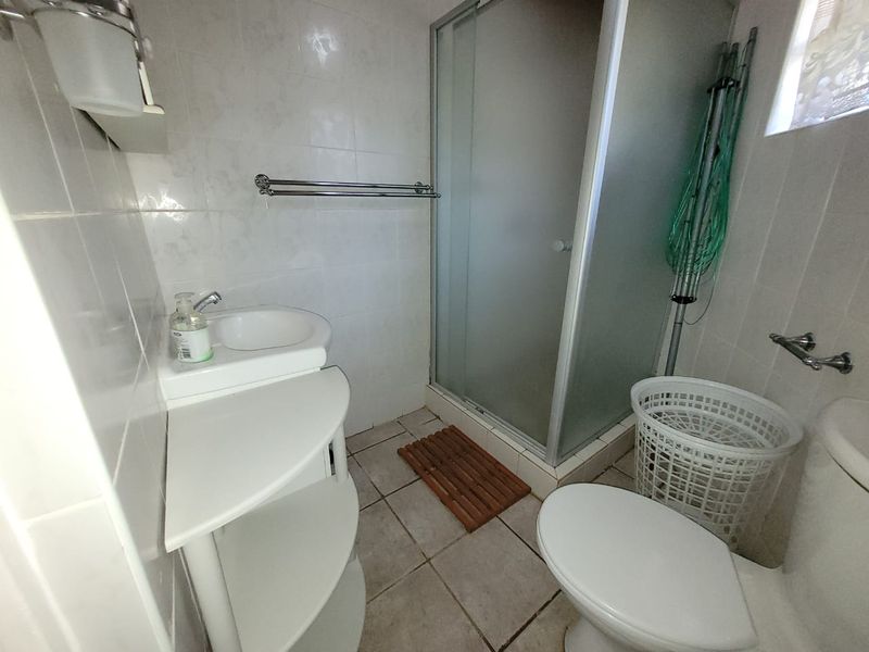 A functional bathroom featuring a shower enclosure, vanity basin, and toilet with neutral tiled finishes throughout.