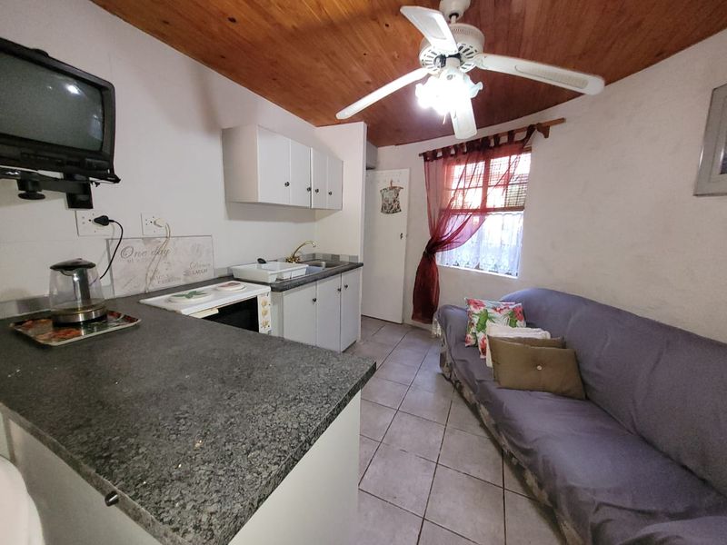 Compact open-plan living area featuring a kitchenette with granite countertops, timber ceiling, and tiled flooring.