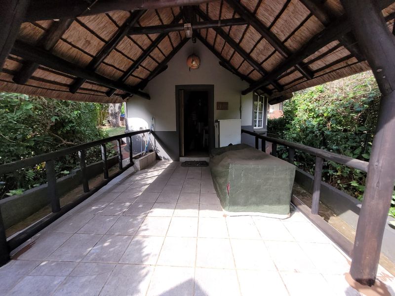 A covered outdoor patio featuring a traditional thatched roof, timber support structure, and tiled flooring, providing a rustic space for outdoor relaxation.