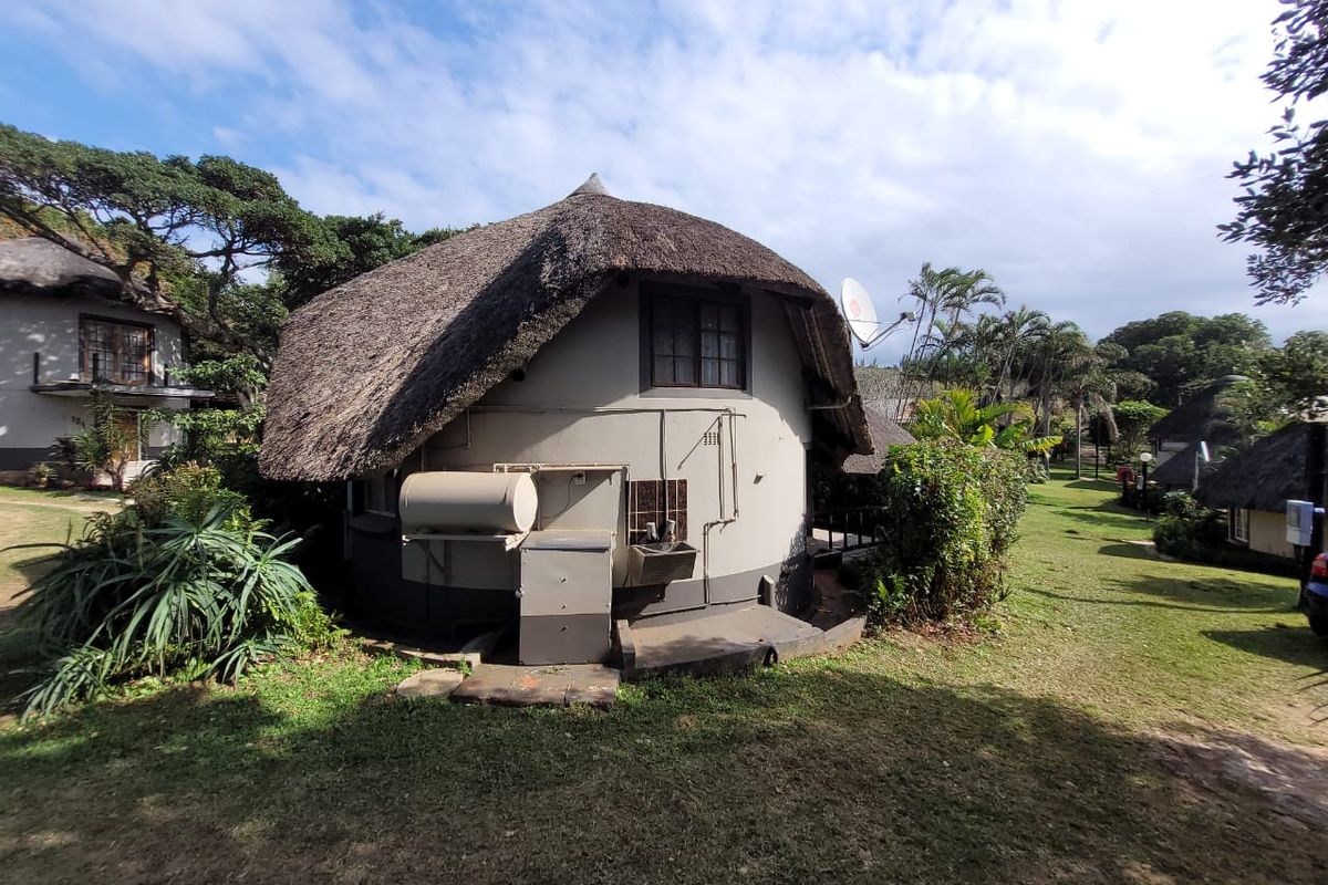 Rear view of a circular townhouse unit featuring a traditional thatch roof, external geyser, and wash basin set within a landscaped estate environment.