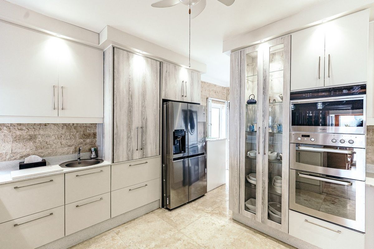 Modern kitchen featuring light wood-grain cabinetry, stone-tiled backsplash, integrated stainless steel oven, and polished stone flooring.