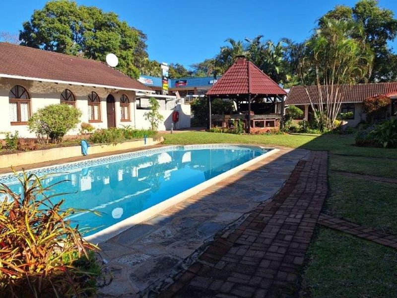 Outdoor pool area featuring a swimming pool, paved walkways, and a covered gazebo set within a landscaped garden environment.