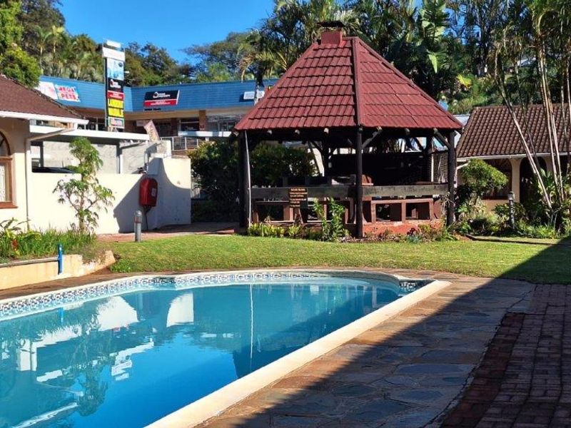 Outdoor pool area featuring a swimming pool, landscaped lawn, and a covered gazebo structure within a communal apartment complex setting.