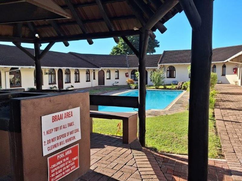 Communal outdoor area featuring a swimming pool, brick-paved courtyard, and a covered thatched gazebo with a built-in braai facility.
