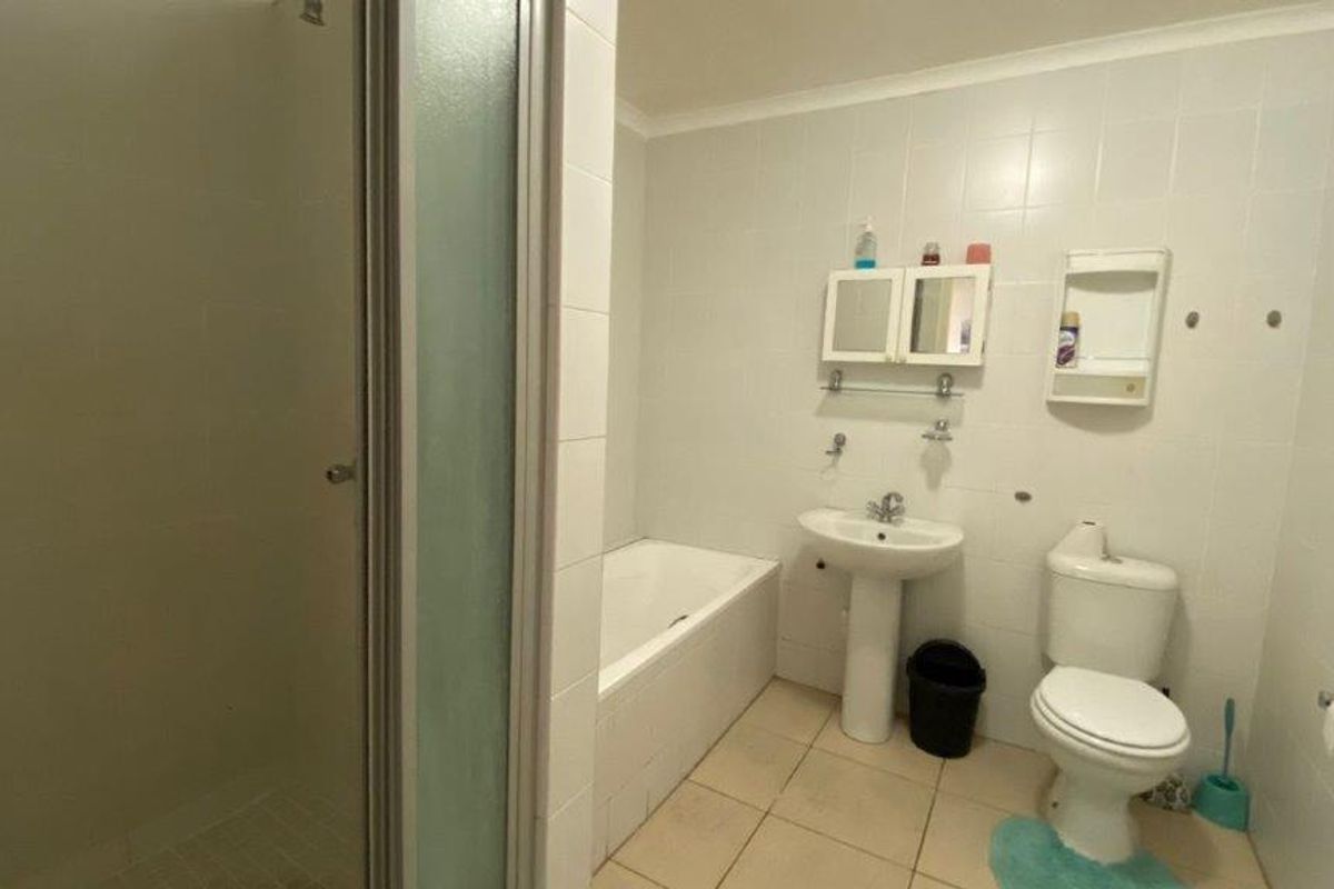 A functional bathroom featuring a separate shower enclosure, bathtub, pedestal basin, and toilet with neutral tiled finishes.