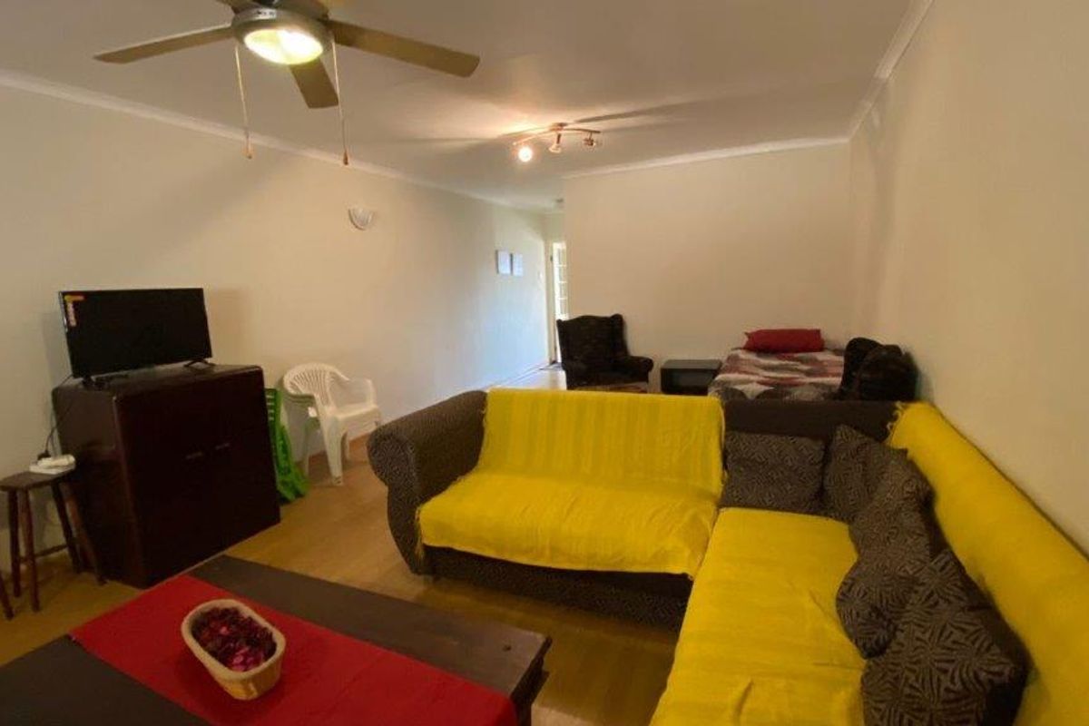 A spacious living room featuring laminate flooring, a ceiling fan, and neutral wall finishes, offering a versatile layout for comfortable daily living.