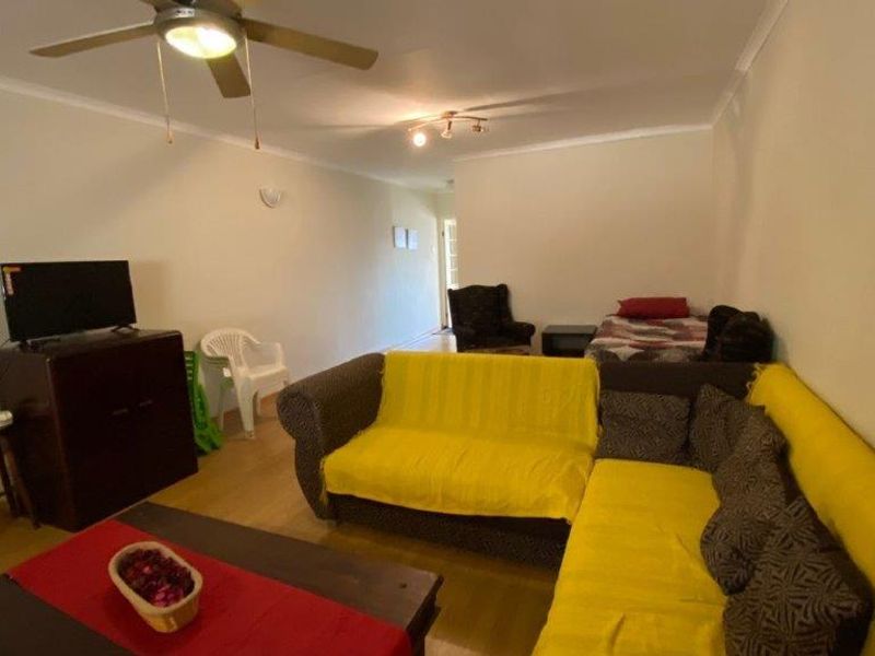A spacious living room featuring laminate flooring, a ceiling fan, and neutral wall finishes, offering a versatile layout for comfortable daily living.