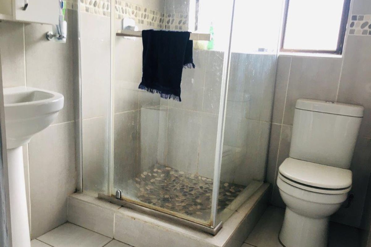 A functional bathroom featuring a pedestal basin, a glass-enclosed shower with pebble flooring, and neutral ceramic wall and floor tiles.