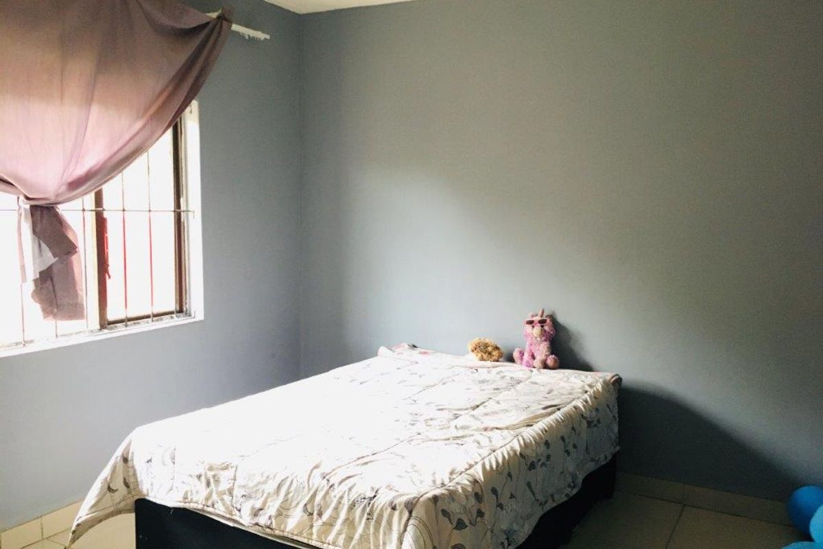 A simple bedroom featuring tiled flooring and a window fitted with security bars.