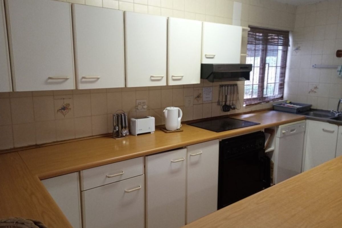 A functional kitchen featuring laminate countertops, built-in cabinetry, an electric hob, and a stainless steel sink, offering a dated but practical layout.