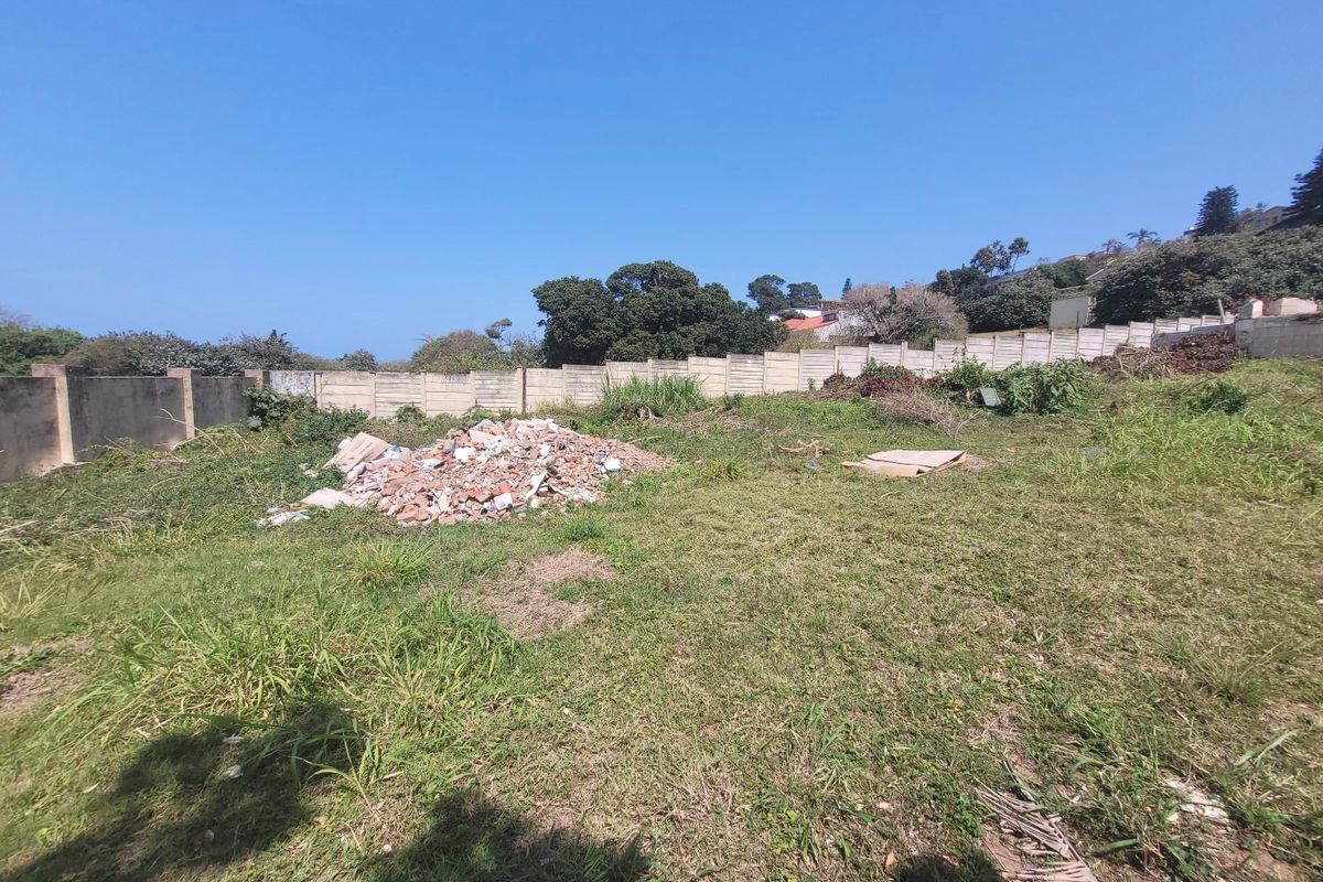 A vacant residential plot featuring a precast concrete boundary wall, currently containing a pile of rubble and overgrown grass.