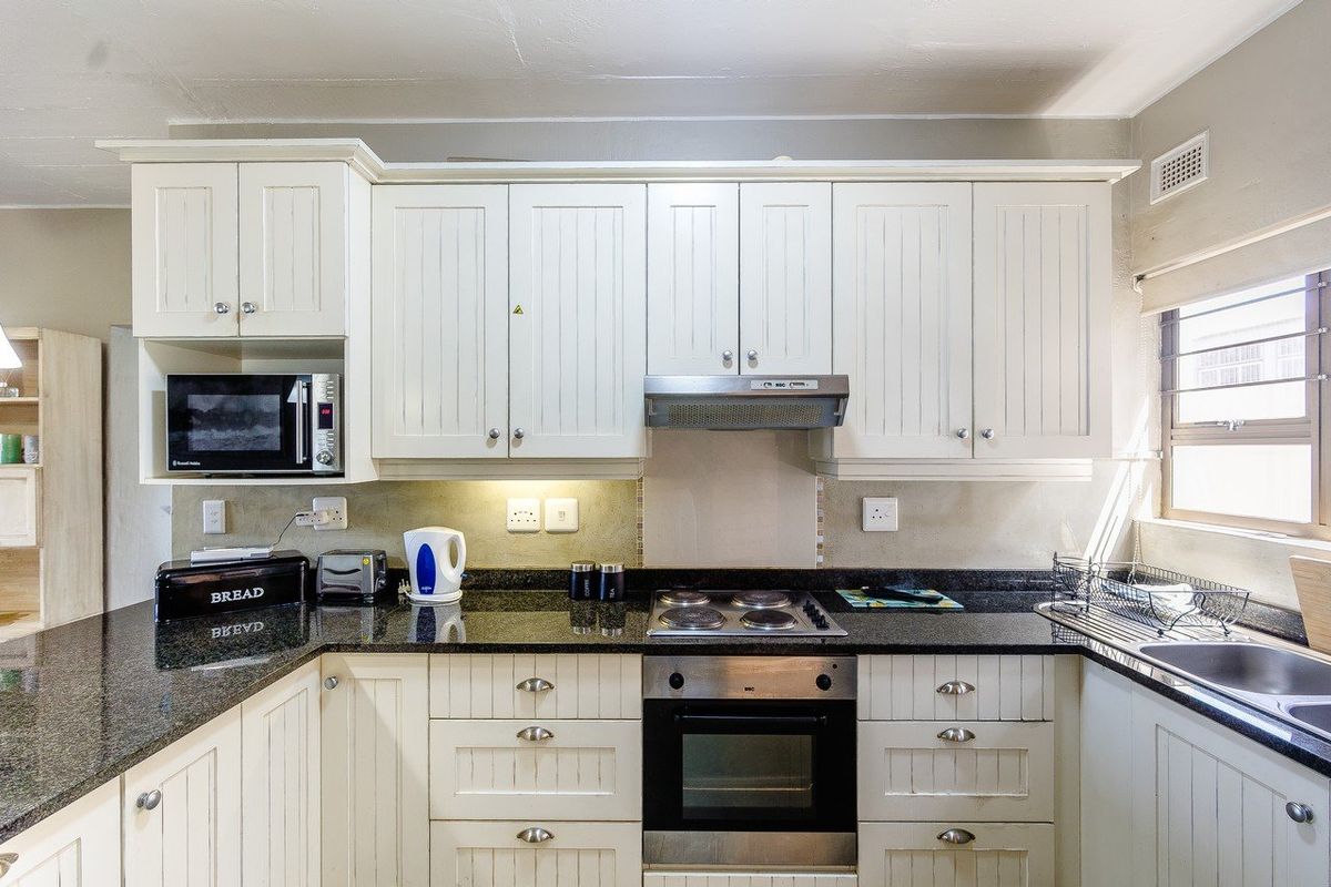 A functional kitchen featuring white shaker-style cabinetry, dark granite countertops, a built-in oven, electric hob, and an integrated microwave.