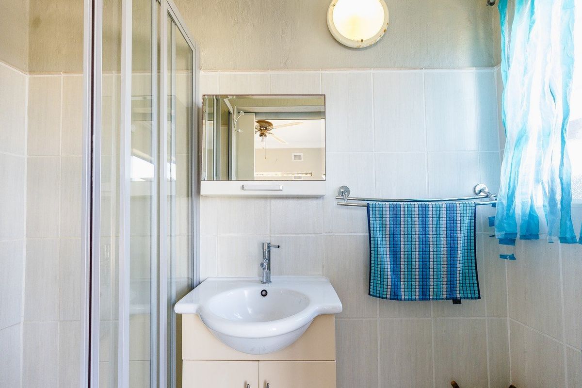 A functional bathroom featuring a shower enclosure, vanity basin with storage, and a wall-mounted mirror cabinet with integrated lighting.