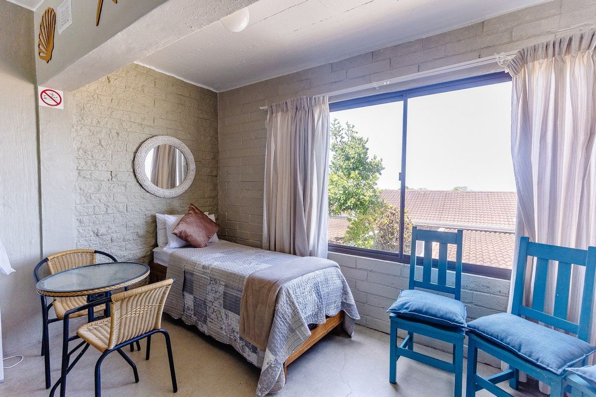 A bedroom featuring exposed brick walls, concrete flooring, and a large window providing natural light and a view of the surrounding area.