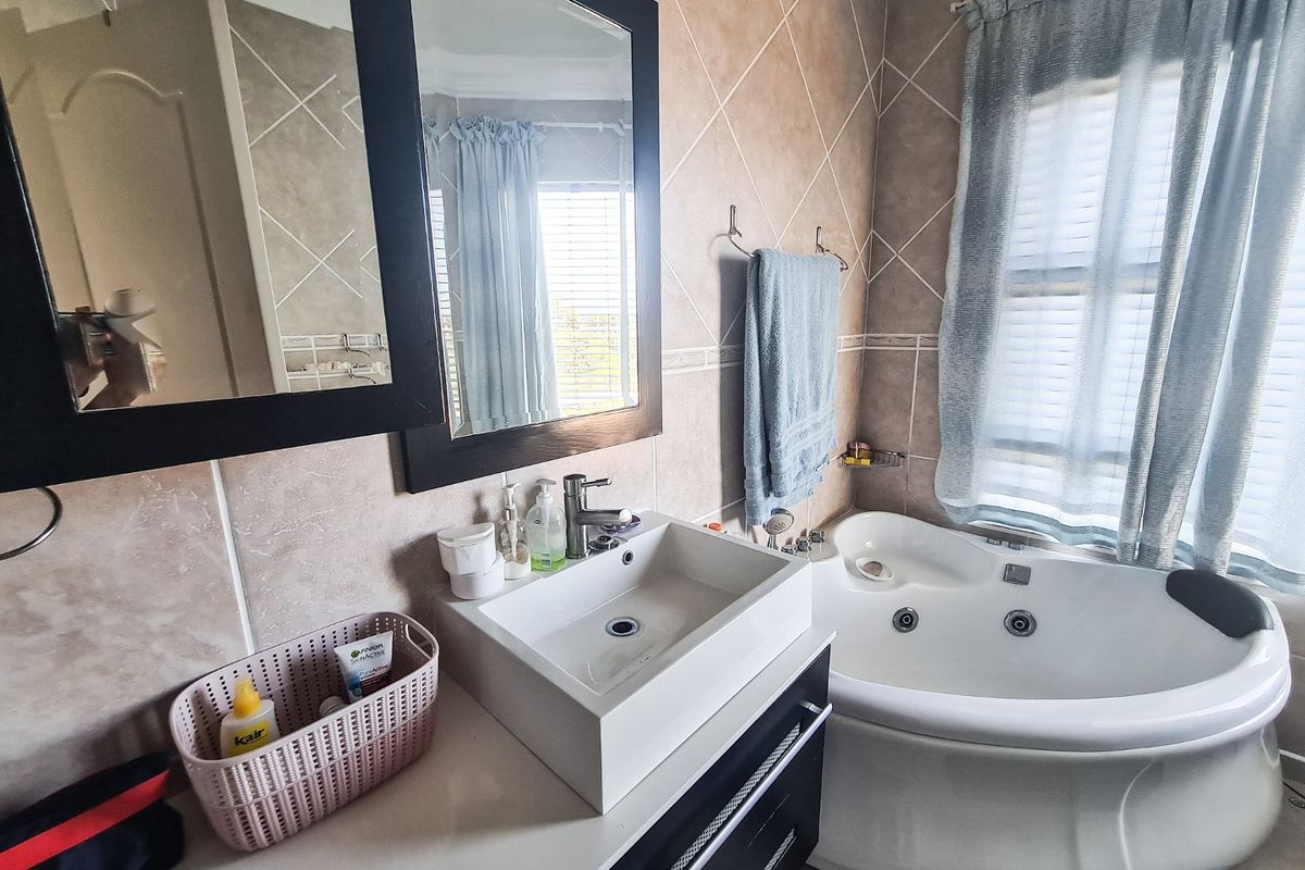 A bathroom featuring a corner jetted bathtub, a modern vessel sink with a vanity cabinet, and neutral ceramic wall tiling.