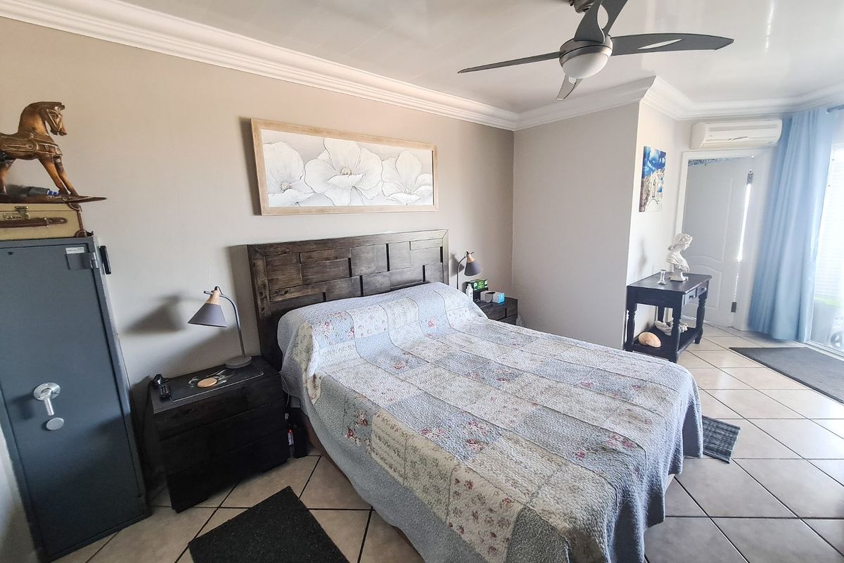A well-maintained bedroom featuring tiled flooring, crown molding, a ceiling fan, and a wall-mounted air conditioning unit.