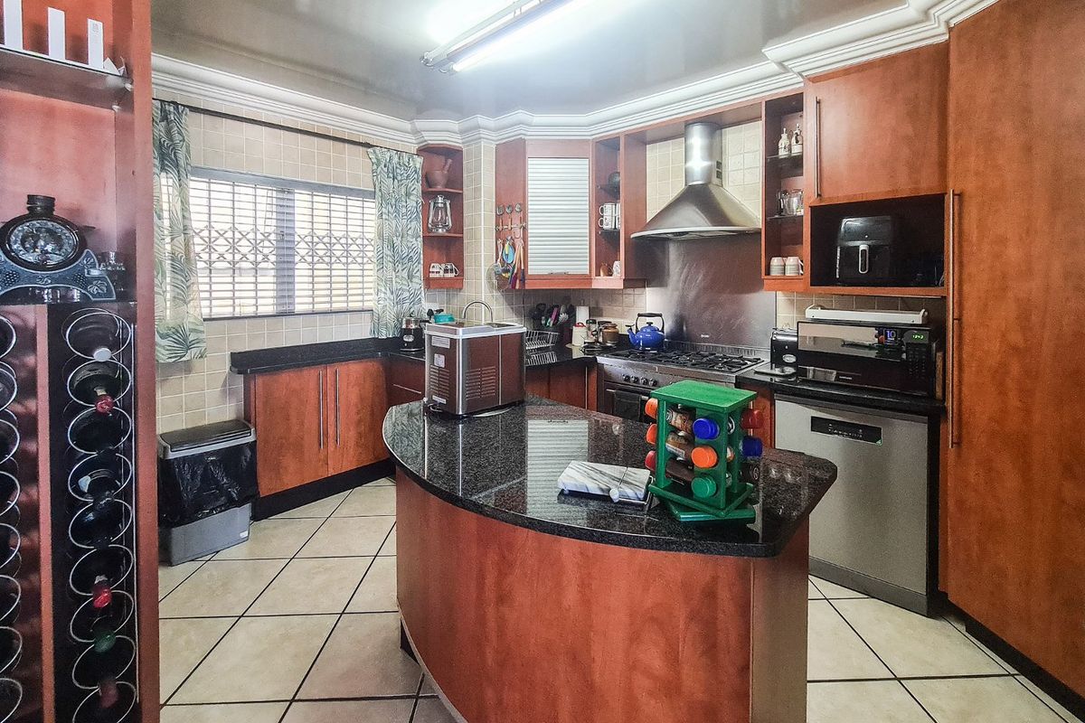 A functional kitchen featuring wood-finish cabinetry, granite countertops, a central island, and built-in stainless steel appliances, including a gas hob and extractor fan.