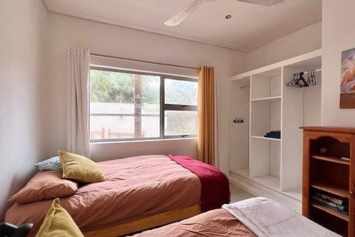 A functional bedroom featuring a built-in wardrobe, ceiling fan, and large window providing natural light.