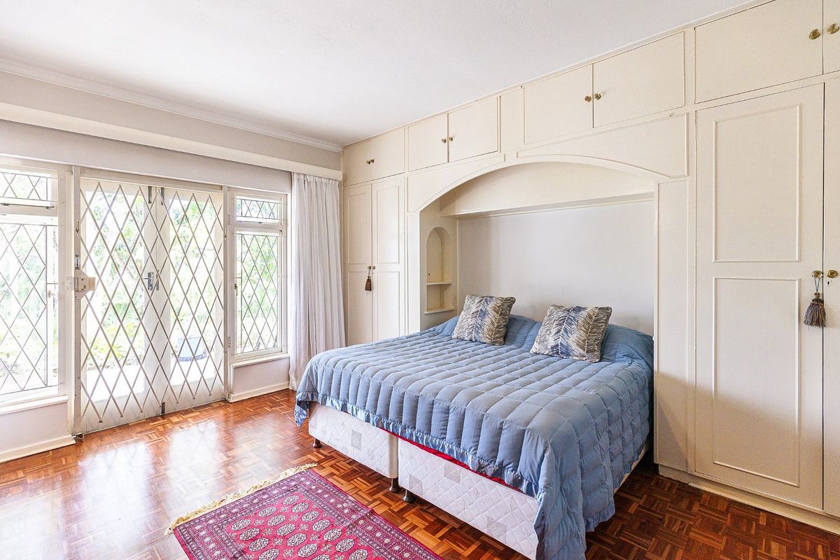 Spacious bedroom featuring classic parquet flooring, extensive built-in cabinetry, and direct access to the garden through secure french doors.