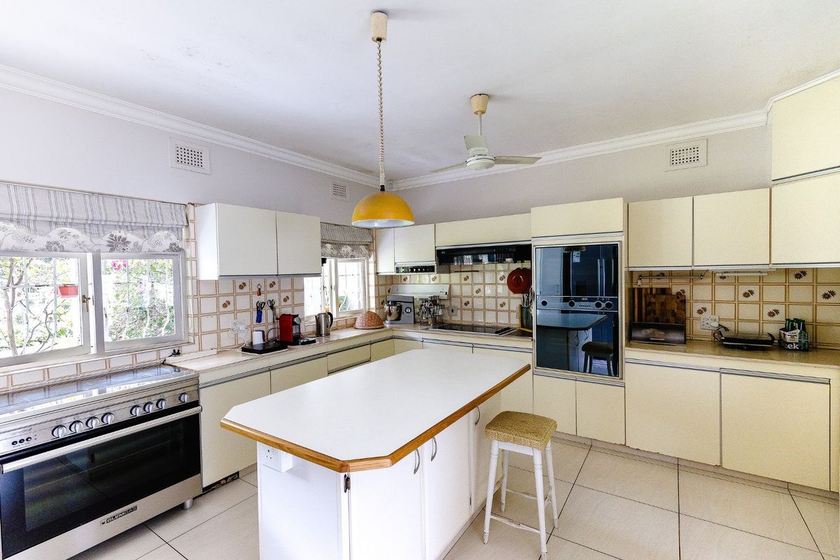 Spacious kitchen featuring a central island, built-in oven, extractor fan, and ample cabinetry, offering a functional layout with classic tiled finishes.