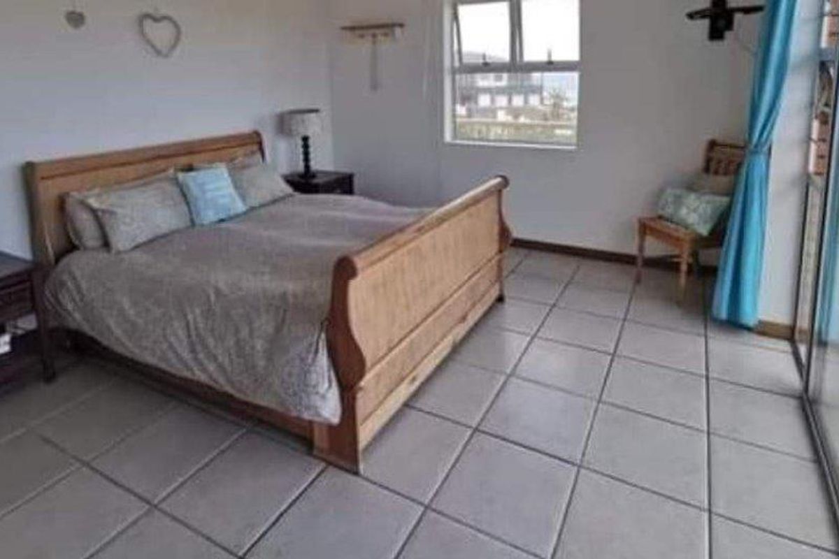 A bedroom featuring tiled flooring, a large sliding glass door providing natural light, and a casement window.