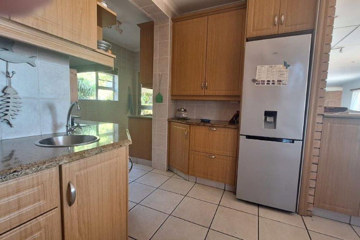 A functional kitchen featuring wood-look laminate cabinetry, granite countertops, a stainless steel sink, and tiled flooring with a connected view to the living area.