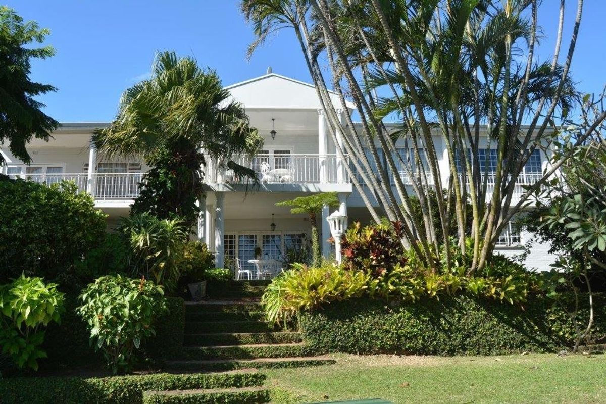 Rear view of a two-story house featuring a balcony, white columns, and a well-maintained landscaped garden with stone steps leading to the patio.