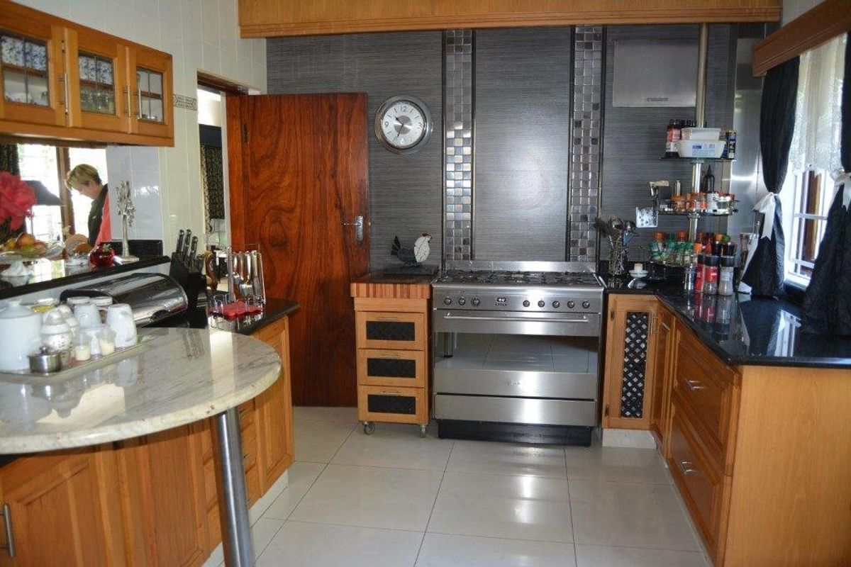A functional kitchen featuring wooden cabinetry, granite countertops, tiled flooring, and a stainless steel gas stove with a tiled splashback.