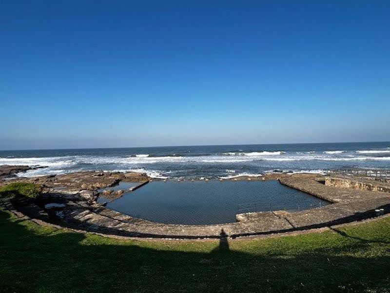 A natural rock pool situated along the coastline, offering direct ocean views and integrated stone landscaping.