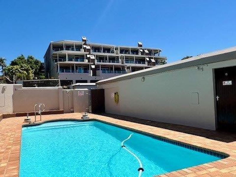 A well-maintained outdoor swimming pool area featuring paved surrounds and boundary walls, set within an apartment complex environment.