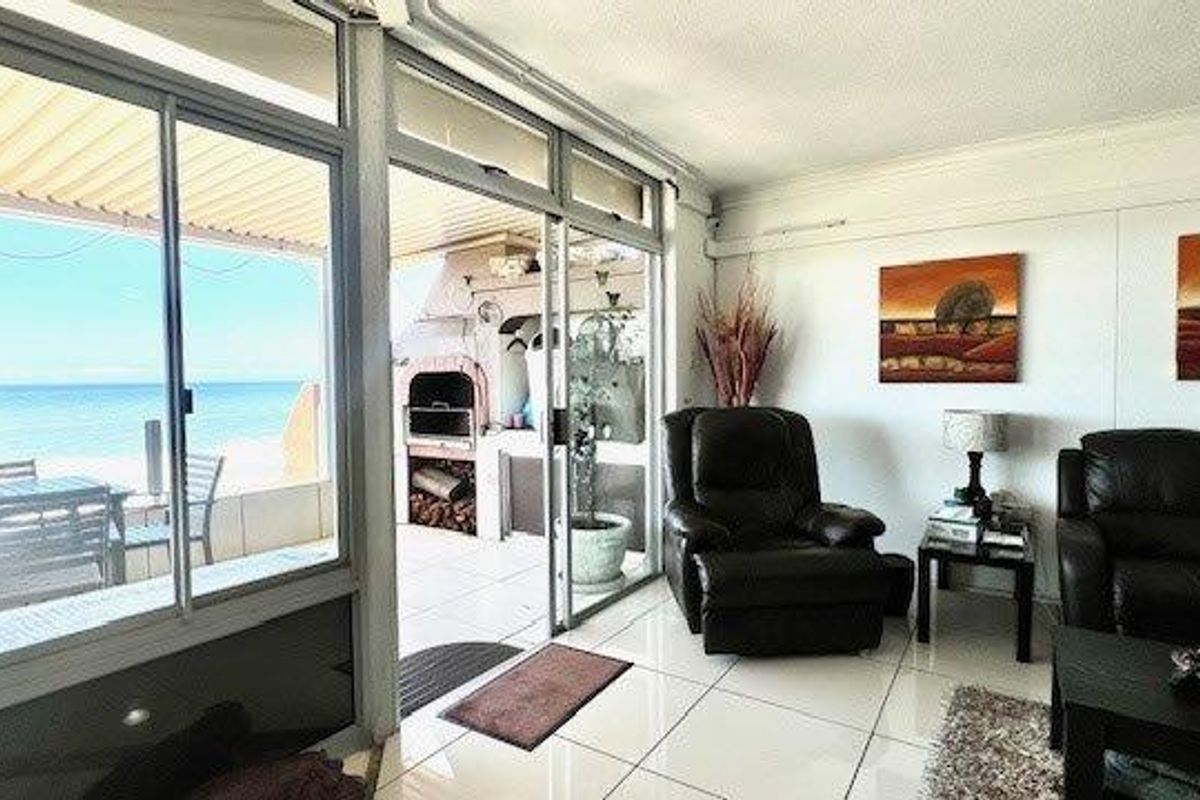Spacious living area featuring large sliding glass doors that open onto a covered patio with a built-in braai and stunning ocean views.