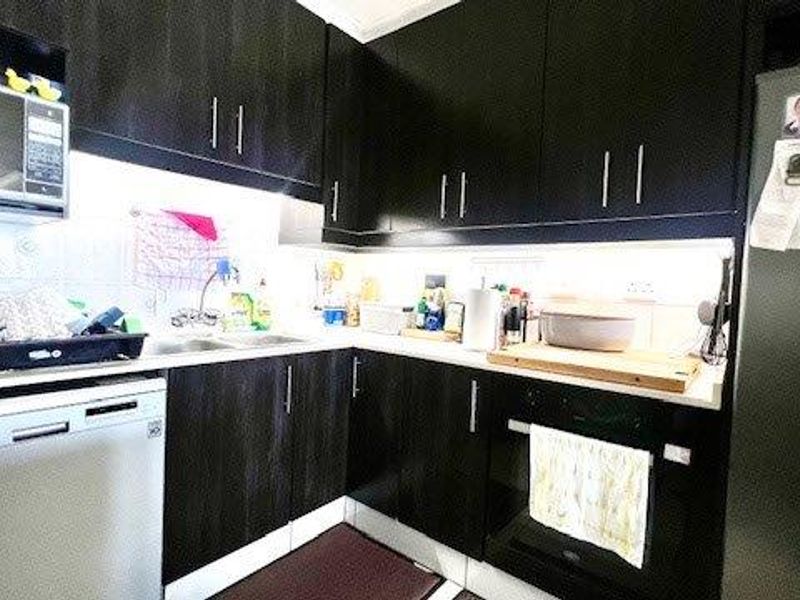 A functional kitchen featuring dark wood cabinetry, a built-in oven, and a tiled splashback with integrated under-cabinet lighting.