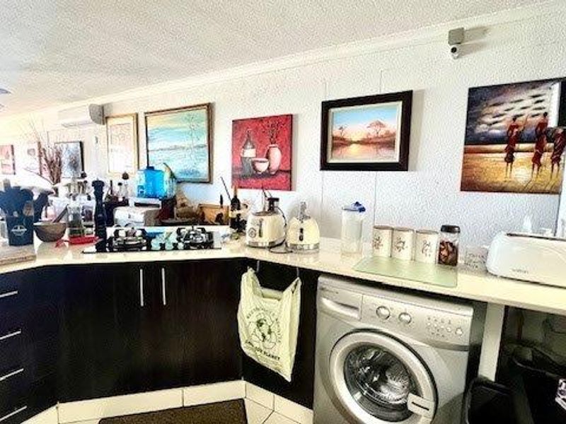 A functional kitchen area featuring dark cabinetry, a gas hob, and an integrated washing machine, with an open-plan layout connecting to the living space.