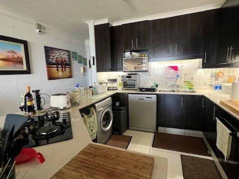 A functional kitchen featuring dark wood cabinetry, stone countertops, a built-in gas hob, and integrated appliances including a dishwasher and oven.