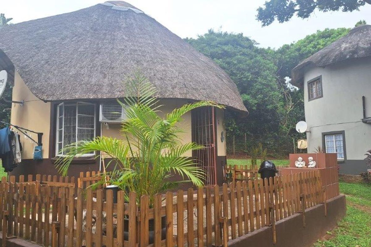 Exterior view of a thatched-roof townhouse unit featuring a small fenced patio area, security gates, and established garden surroundings.