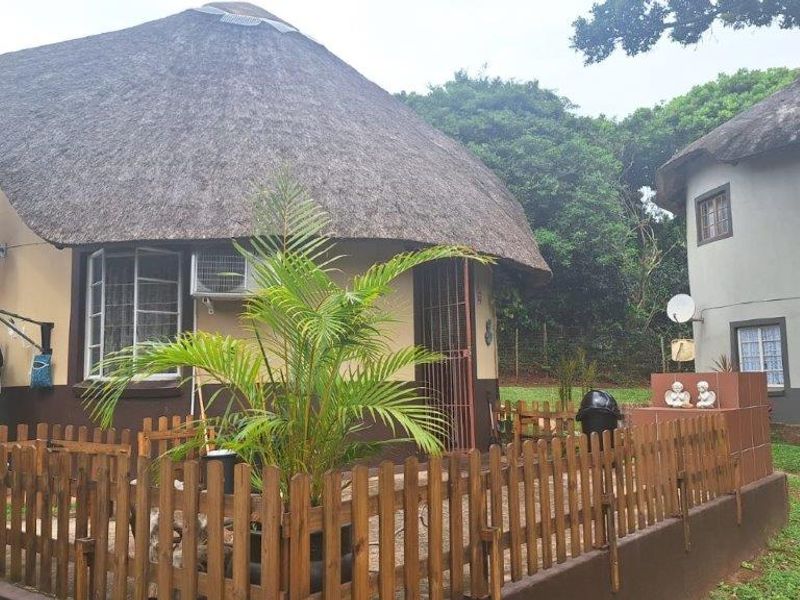 Exterior view of a thatched-roof townhouse unit featuring a small fenced patio area, security gates, and established garden surroundings.