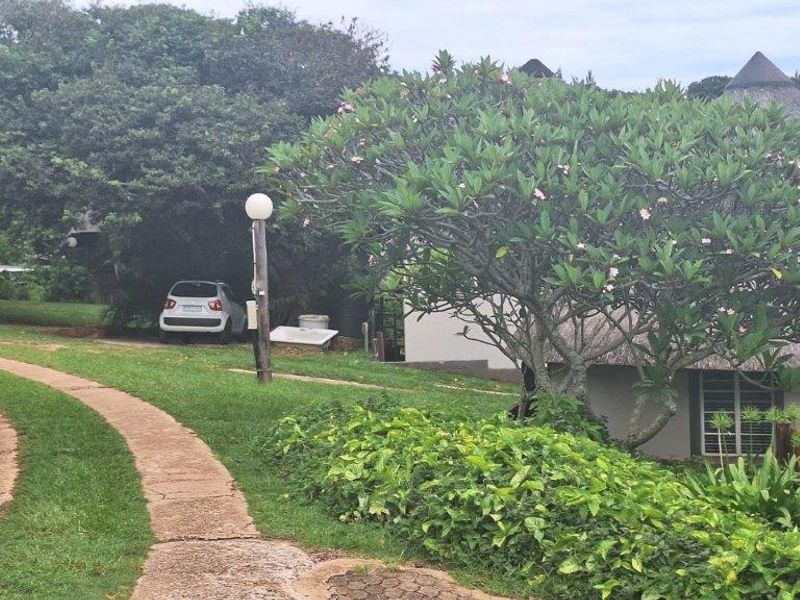 Front view of a townhouse featuring a traditional thatched roof, paved driveway, and established garden surroundings.