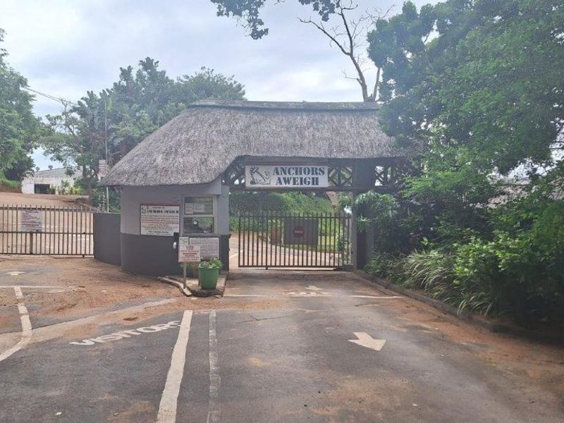 The entrance to the Anchors Aweigh complex featuring a gated security access point with a traditional thatch roof structure.