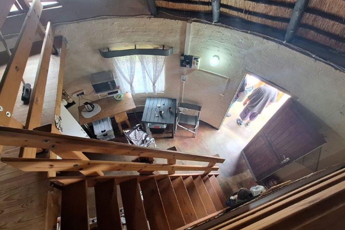 An elevated view of a rustic living area featuring exposed brick walls, a traditional thatch roof, and a timber staircase.
