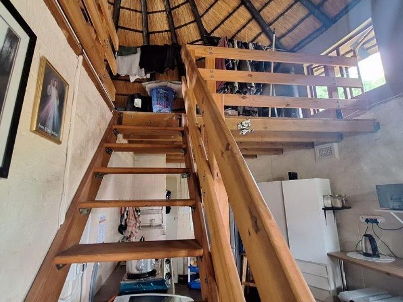 Open plan living area featuring a mezzanine level with timber staircase and exposed thatch roof structure.