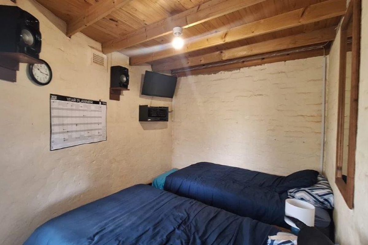 A rustic bedroom featuring exposed timber ceiling beams and painted brick walls, offering a unique character-filled space.