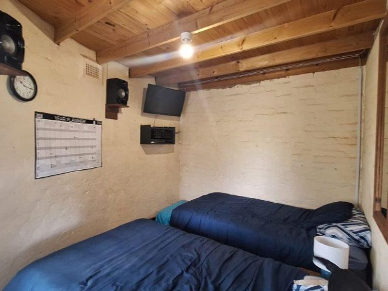 A rustic bedroom featuring exposed timber ceiling beams and painted brick walls, offering a unique character-filled space.