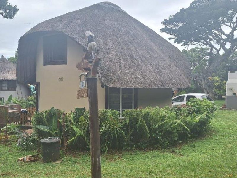 A view of a townhouse exterior featuring a traditional thatched roof, plastered walls, and a private garden area with an outdoor fireplace.