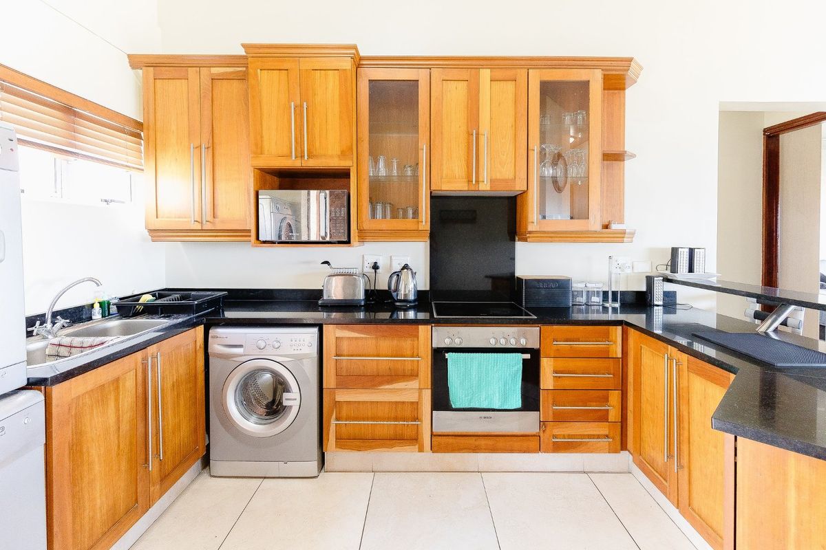 A well-maintained kitchen featuring warm wooden cabinetry, black granite countertops, integrated oven, electric hob, and tiled flooring with a functional layout.