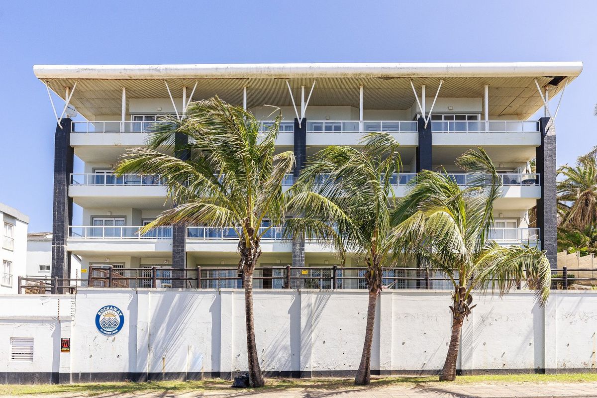 Rear elevation of a multi-story apartment building featuring private balconies with glass railings and a secure perimeter wall.