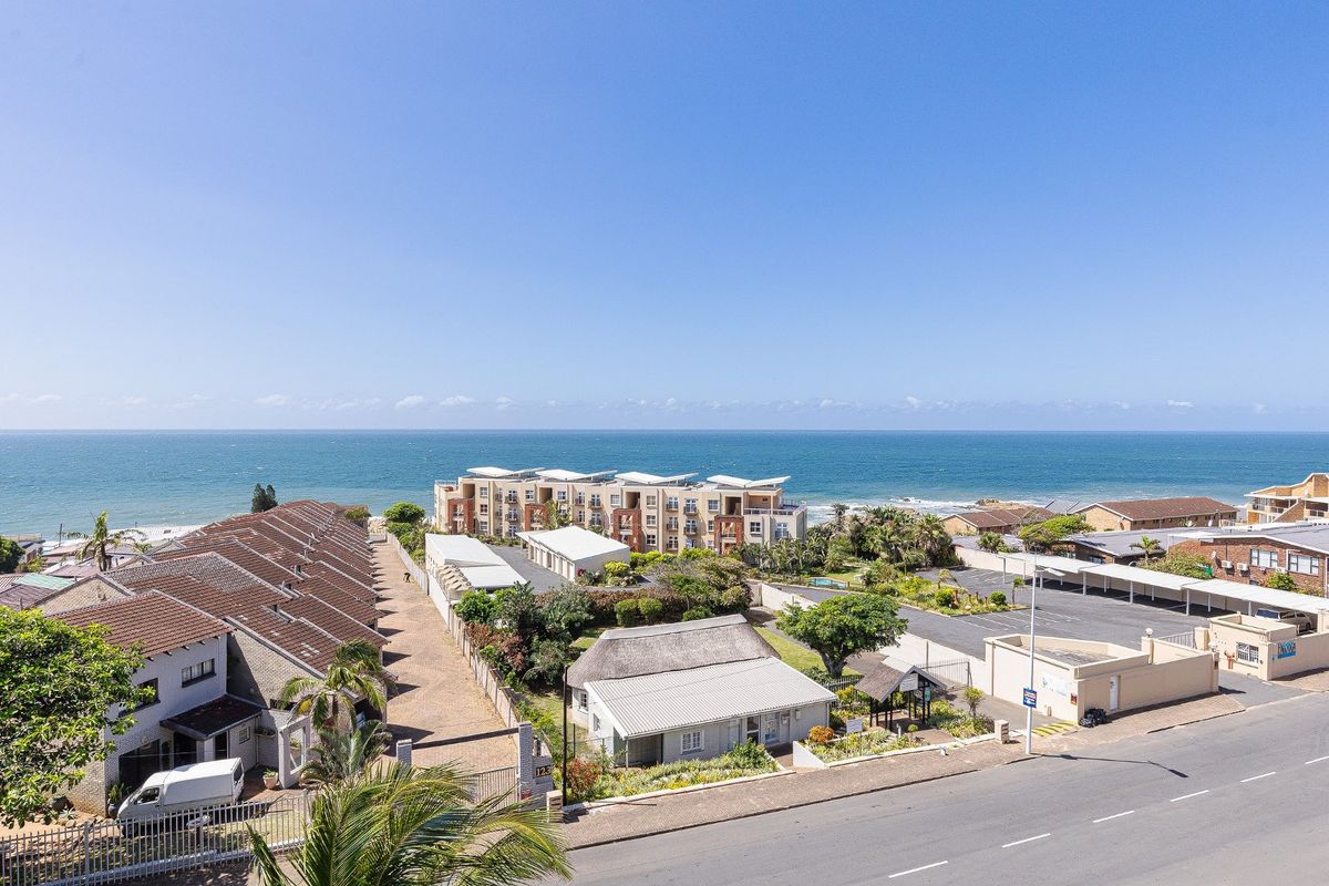 An elevated aerial view of the coastal apartment complex, showcasing the surrounding neighborhood, parking facilities, and proximity to the ocean.
