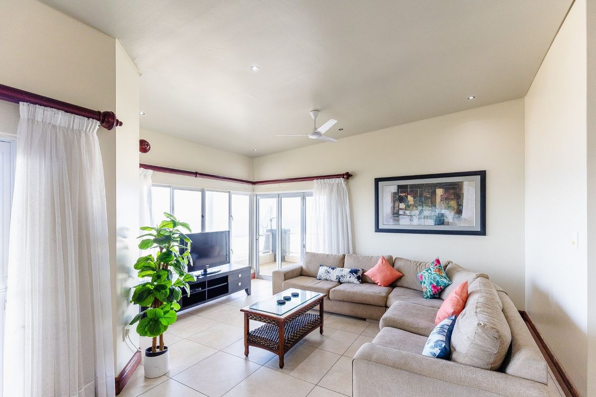 A bright and spacious living room featuring tiled flooring, a ceiling fan, and large sliding glass doors that provide ample natural light.