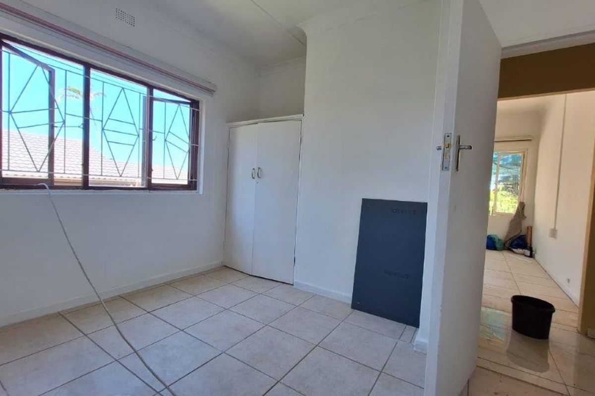 An empty bedroom featuring tiled flooring, a built-in wardrobe, and security bars on the window, requiring minor cosmetic updates.